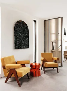 Two mustard-colored armchairs with wooden frames and a textured red side table in a modern interior design setting.