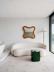 Modern living room featuring a sleek, curved sofa upholstered in a light beige fabric, a white marble floor, and a green meta