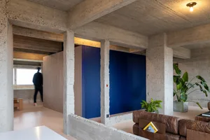A modern minimalist interior features a blue wall and exposed concrete beams and pillars.