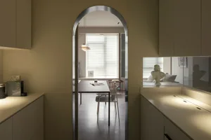 A minimalist residential space with neutral tones and an open layout, featuring a dining table and chairs, a kitchenette, and