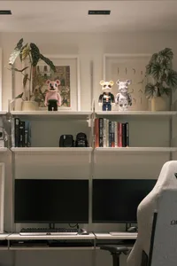 Home office with eclectic shelves displaying books, plants, and figurines, along with two computer monitors and a gaming chai