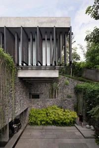 An exterior view of a modern architectural house with concrete walls and a greenery garden.