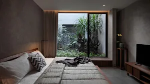 Modern bedroom with concrete walls, a large bed, and a garden view.