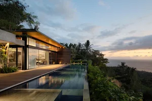 Modern house with glass walls and wooden deck overlooking ocean.