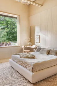 A minimalist bedroom featuring neutral colors with a large window overlooking greenery and a small workspace area.