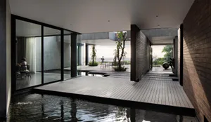Modern residential living room with glass walls, wood floor, and concrete columns overlooking an outdoor space.