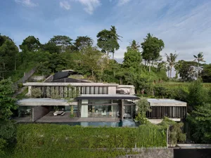 Modern residential house with a concrete and glass exterior on a green hillside.