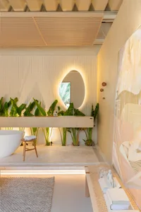 A minimalist bathroom with concrete walls, a white tub, and plants in front of a large mirror.