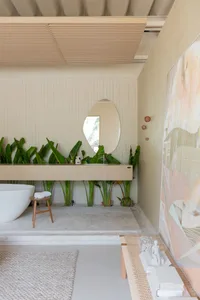 A minimalist bathroom with a wooden vanity, concrete floor, and lush green plants