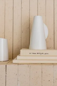 A minimalist ceramic vase sits atop a stack of books on a wooden shelf.
