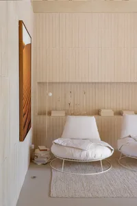 A minimalist living room featuring white upholstered chairs, a wooden floor, and a concrete wall.