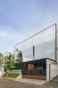A modern house with glass panels and a wooden entrance gate, featuring a glass wall and a garden with plants.