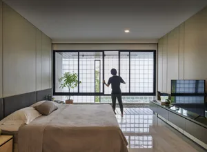 A person standing in a modern minimalist bedroom with large glass windows, looking outside.