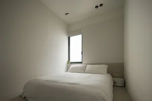 A minimalist bedroom featuring a large bed with white bedding and a neutral color palette.