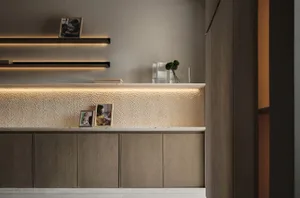 A modern minimalist wooden desk with a textured surface, illuminated by subtle lighting, featuring framed photos and greenery