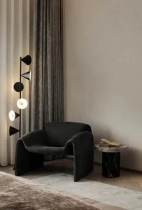 A modern bedroom featuring a black leather armchair, a marble side table with books, and a floor lamp with multiple shades.
