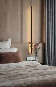 A modern bedroom with a bed, white and brown pillows, grey curtains, and a hanging light fixture.