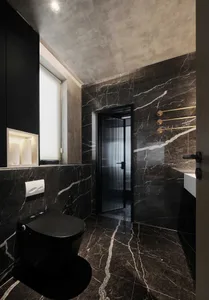 A modern bathroom with dark marble walls and floor, a sleek black toilet, and a glass door.