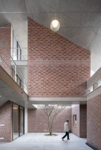 A modern industrial courtyard building with brick and concrete materials and a central tree.