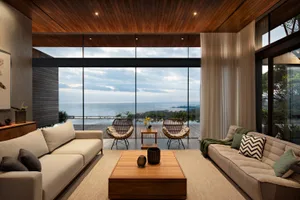 A modern living room with wooden flooring, glass walls, and beige sofas with patterned cushions.