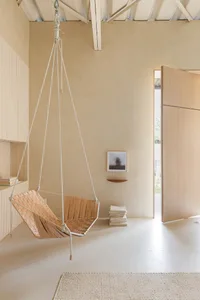 A minimalist room featuring a hanging swing seat made of wood and leather