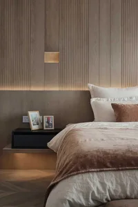 A modern bedroom with wood paneling, featuring a neatly made bed with soft bedding and a floating nightstand with framed pict