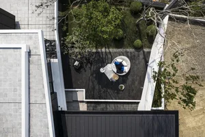 Modern residential patio with wooden deck and outdoor furniture, surrounded by greenery and trees.