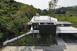 A modern house with a concrete exterior and greenery around it.