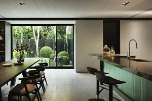A modern kitchen with wooden flooring, a long wooden dining table, black chairs, and a kitchen island with a green countertop