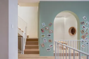 A wooden staircase with a railing, framed photos on the wall, and a table with chairs.
