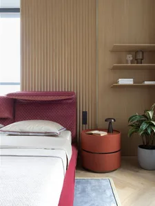 A minimalistic bedroom with a red velvet bed frame, wooden wall, and a circular bedside table with a plant.