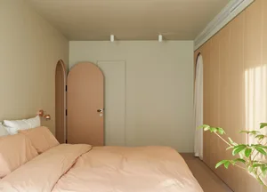 A minimalist bedroom with neutral-colored walls, a peach-colored bedspread, and a plant in a pot.