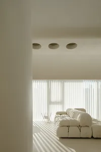 A minimalist interior featuring a white sofa and vertical blinds.