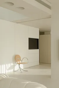 A minimalist living room with neutral colors, featuring a sleek design chair and a flat-screen TV.