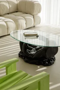 A modern living room featuring a transparent black table and green wooden chairs with sunlight filtering through the window.