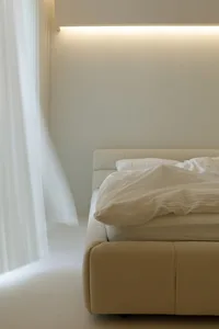 A minimalist bedroom with neutral-toned upholstery, illuminated softly by a concealed light source.