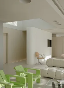 A modern living room featuring a modular sofa with green accents and neutral-colored surroundings.