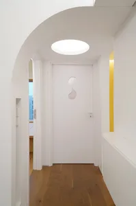 A modern white corridor features an arched wooden door with a unique cutout design and a circular light fixture in the ceilin