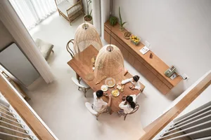 Family gathered together in a modern residential dining room with elegant wood and cane furniture, enjoying a meal with fruit