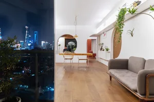 Modern living room at night featuring wooden flooring and glass wall overlooking cityscape.