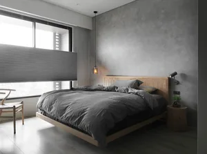 A minimalist bedroom with concrete walls, a wooden bed frame, and gray bedding.