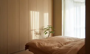 A minimalist bedroom with a textured wooden bed and window allowing soft light to filter in.