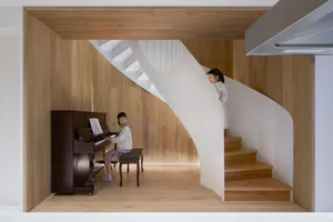 A modern music studio featuring a wooden staircase and a woman playing the piano.