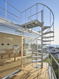 Modern residential home featuring glass, steel, and wood materials, with spiral staircase and outdoor balcony overlooking a c