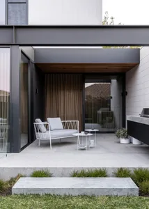 Modern industrial outdoor lounge area featuring a white metal chair with light grey cushions, a metal coffee table, and potte