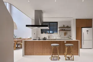 A modern, minimalist kitchen featuring wood cabinets, white ceramic countertops, and stainless steel appliances and fixtures.
