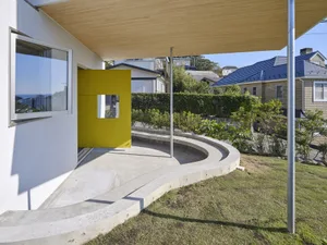 Modern backyard with concrete patio, yellow geometric wall, and greenery.