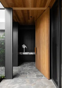 Modern entrance with wooden door and stone flooring, showcasing contemporary design elements.
