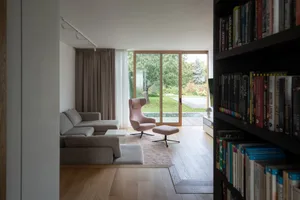 A modern living room featuring a bookshelf filled with books, a grey sectional sofa, and a pink lounge chair.