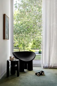 A minimalist room with a modern, sleek black sofa made of concrete, situated in front of a large window with a white curtain,